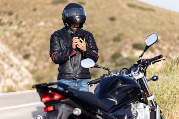 Foto de motociclista hombre hablando por teléfono con el seguro de su motocicleta después de haber sufrido una avería en la carretera. | Foto Premium