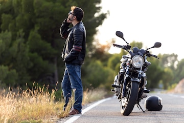 Foto de motociclista hombre hablando por teléfono con el seguro de su motocicleta después de haber sufrido una avería en la carretera. | Foto Premium
