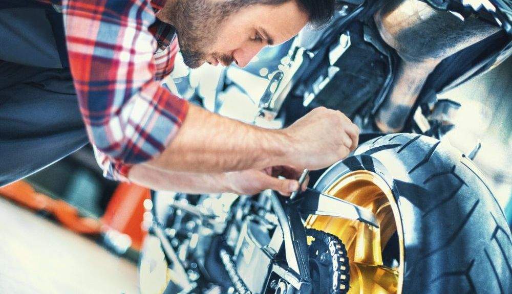 Profesional revisando una de las llantas de una moto. Fuente: iStock / gilaxia